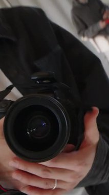 Meslektaşı ya da asistanla çalışarak geniş güneş ışığı stüdyolarında fotoğraf çekerken büyük objektifli profesyonel kamera kullanan beyaz erkek fotoğrafçının dikey el kamerası görüntüsü.