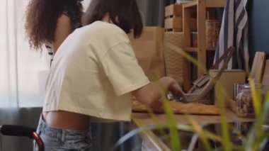 Serebral felçli beyaz bir kız ve melez kız arkadaşının alışveriş yaptıktan sonra mutfak masasında kağıt torbaları açarken sohbet ederken orta boy fotoğrafı.