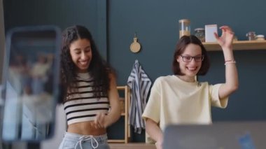 Sosyal medya için serebral felçli dans videosu çeken neşeli, beyaz bir genç kızın akıllı telefondaki çift cinsiyetli kız arkadaşıyla boş zamanlarını evde geçirirken çekilmiş orta boy fotoğrafı.
