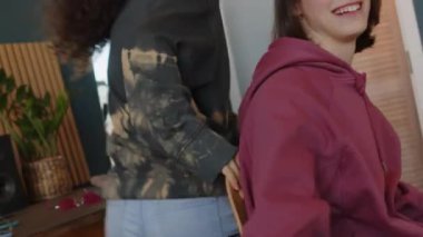 Serebral felçli neşeli beyaz bir kızın Melez kız arkadaşının parlak, modern apartman dairesinde onu sandalyeye oturturken 2k gözlük takıp gülüşünü çekmek.