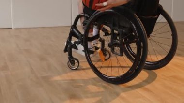 Tekerlekli sandalyeli, kapalı sahada basketbol topu sektiren, kararlı, beyaz, dövmeli bir sporcu.