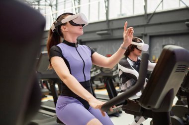 Fütüristik spor salonu fotokopi alanında egzersiz bisikletinde çalışan genç bir kadının yan görünüm portresi