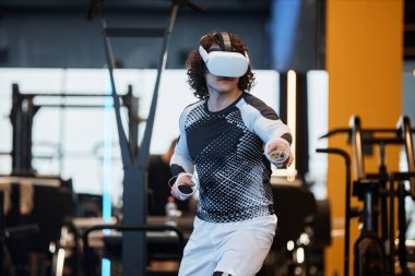 Spor salonunda VR kulaklık takan ve çeviklik eğitimi alan bir adamın belden yukarı portresi.