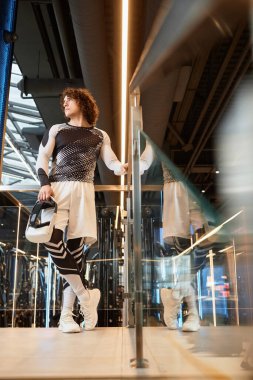 VR kulaklık takan sportif bir gencin dikey boy portresi. Fütürist spor salonunda ayna ile yansıtmalı poz veriyor.