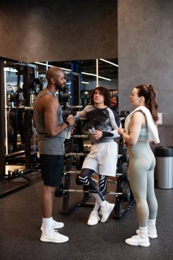 Spor salonunda sohbet eden üç sporcunun dikey boy portresi. Eğitimde mola veriyorlar.