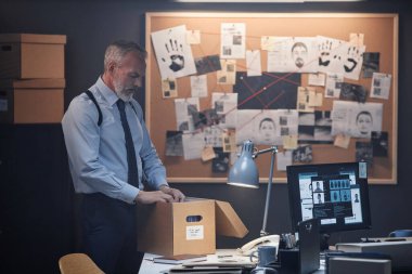 Ofiste dikilirken dosyalara bakan sakallı kıdemli dedektifin yan görünüm portresi.