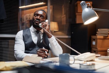 Afrika kökenli Amerikalı bir erkek dedektifin portresi ofis telefonuyla konuşuyor, boşluğu kopyala