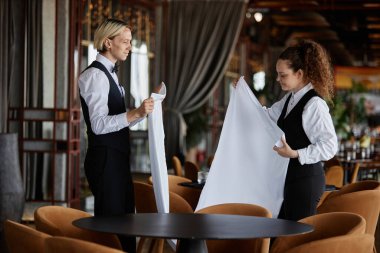Lüks restoranı açılışa hazırlarken beyaz masa örtüleri tutan iki genç sunucunun yan görünüm portresi, boşluğu kopyala