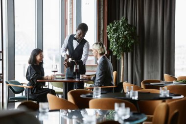 Lüks restoranın içinde bir çift akşam yemeği yiyor ve bardaklara kırmızı şarap dolduruyor.