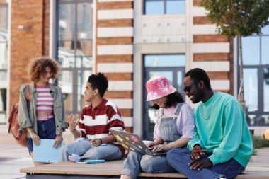 Üniversite kampüsündeki çeşitli genç üniversite öğrencileri dizüstü bilgisayar kullanarak gülümseyen bir çifte odaklanıyor.