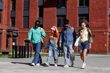 Modern üniversite kampüsünde gün ışığıyla aydınlanan çok ırklı genç öğrencilerden oluşan bir gruba geniş bir bakış açısı.