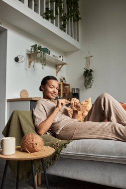 Evdeki kanepede rahat rahat otururken örgü ören genç Afrikalı Amerikalıların dikey portresi.