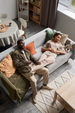 Genç Afrikalı Amerikalı bir çiftin rahat evlerinde kanepede kestirirken yüksek açılı portresi.
