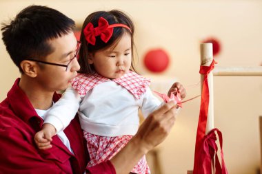 Asyalı bir babanın Çin Yeni Yıl kutlamaları için evi dekore eden tatlı küçük bir kızla yan görünüm portresi.