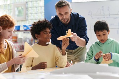 Öğretmen sınıfındaki öğrenciler tarafından yapılan uçak modellerini kontrol ediyor.