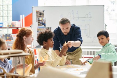 Öğretmen, öğrencinin sınıfta yaptığı uçak modelini geliştirmesini istiyor.