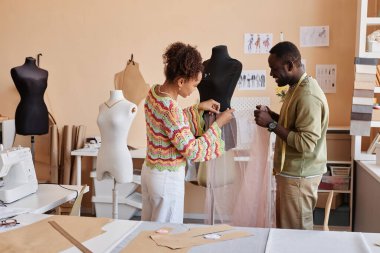 İki genç Afrikalı Amerikalı terzinin elinde bir parça yağ mankeni, biri iş sırasında kumaş iğnelerken.