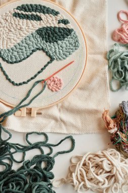 Piece of white canvas with fragment of handmade embroidery clamped in hoop lying on workplace of creative designer or fashion stylist