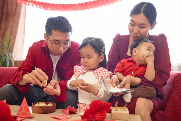 stock image Portrait of happy Chinese family with two children celebrating New Year together at home, all wearing red and opening fortune cookies