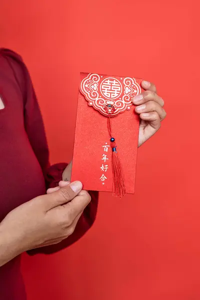 stock image Closeup of woman holding ornate hongbao envelope against red background as Chinese new year tradition Have overflowing abundance every year
