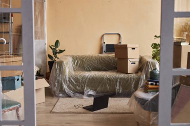 Dizüstü bilgisayar, kanepenin yanında duruyor. İçinde ev malzemesi dolu karton kutular var.