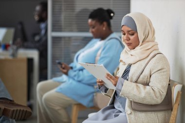 Vize talep merkezinde müdürlük kuyruğunda oturan tesettürlü genç Müslüman kadın