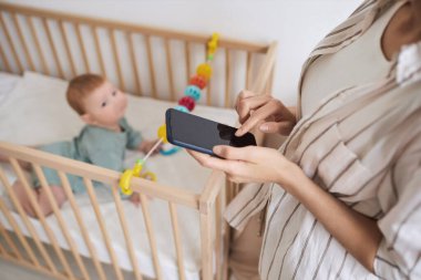 Yüksek açı, elinde akıllı telefon tutan ve internette çocuk bakımı tavsiyesi arayan tanınmayan genç bir annenin görüntüsü.