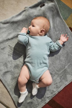 Güneşin altında yumuşak bir battaniyeye uzanmış ve emzik emen tatlı erkek bebek manzarası.