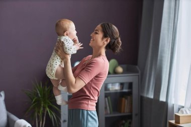 Bebek tutan ve anneliğin tadını çıkaran mutlu genç bir kadının yan görüntüsü.