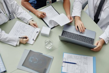 Doktorların klinikteki masada toplanıp hastaların durumunu tartışmalarının üst görüntüsü.