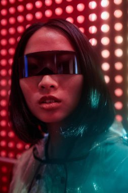 Kırmızı sette siber punk gözlük takan Asyalı genç bir kadının dikey yakın plan portresi.
