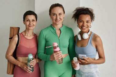 Spor kıyafetleri giyen ve spor salonunda kameraya gülümseyen bir grup kadın.