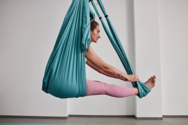 Hamakta esneme egzersizleri yapan ve hava yogasından zevk alan genç bir kadının yan görüntüsü.