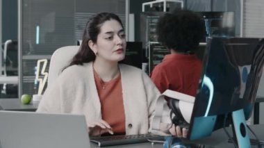 Orta Doğulu kadının bilgisayarını kullanırken VR kulaklığını elinde tutarak modern bilişim ofisinde siyahi bir bayan meslektaşıyla çalışmasının belini kaldır.