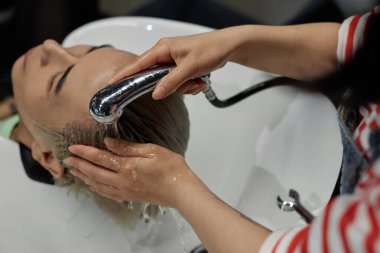 High angle closeup of hairstylist carefully washing hair of male client in beauty salon sink clipart