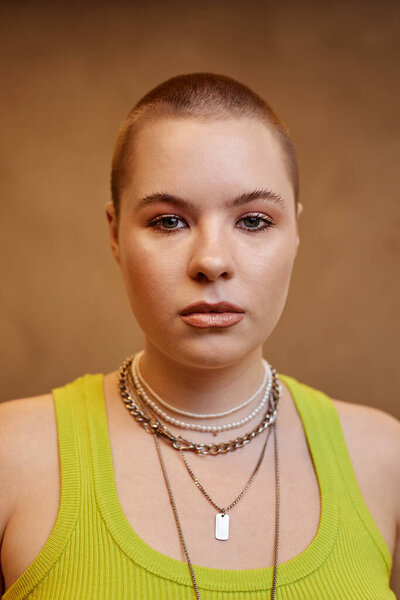Vertical close up portrait of confident young woman with buzzcut looking at camera in studio