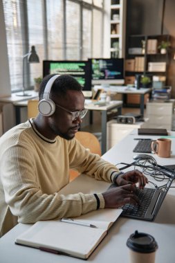 Genç Siyah yazılım geliştiricisi yeni açılan şirketin ofisinde dizüstü bilgisayarda çalışıyor.