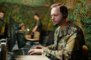 Kulaklıklı genç ciddi bir erkek operatör bilgisayar ekranındaki grafik verilere bakıyor ve klavye tuşlarında parmak uçlarını tutuyor