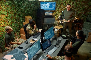 Kültürler arası genç memurlar izleme odasındaki bilgisayar ekranlarının önünde oturuyorlar ve kendilerine güvenen bir adamın rapor vermesini dinliyorlar.