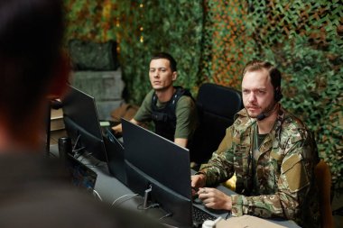 Gözetleme ofisinin genç ve ciddi erkek operatörü bilgisayar başında otururken hoparlöre ya da meslektaşına bakıyor.