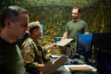 Tişörtlü genç bir erkek polis memuru gizli belgelerle birlikte kamuflaj üniformalı çok ırklı kadın meslektaşlarına geçiyor.