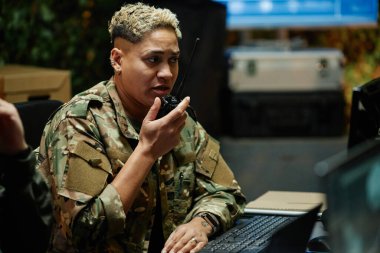 Bir şey rapor ederken ve bilgisayar ekranına bakarken telsiz kullanan çok ırklı genç bir kadın gözetleme memuru.