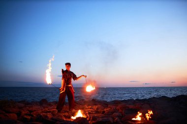Sahilde ateşli poi dansı yapan erkek ateş gösterisi sanatçısının geniş açılı görüntüsü, boşluğu kopyala