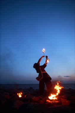 Gece gökyüzüne karşı ateşle dans eden genç bir adamın dikey portresi.