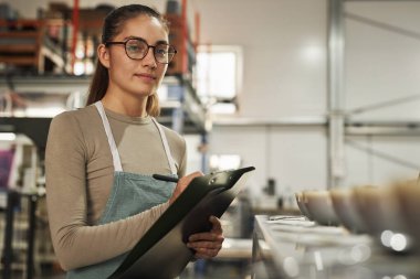 Kahve fabrikasındaki kupa çekme ve kalite kontrolü sırasında not alan kahve uzmanı genç kadın portresi.