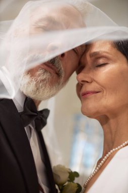 Düğün günü peçeyle kaplı, sevgi dolu yaşlı bir çiftin düşük açılı portresi.