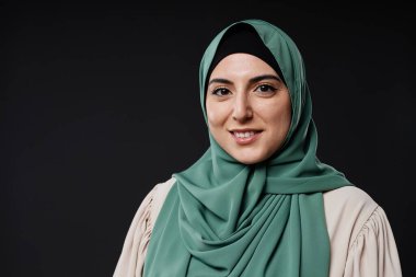 Siyah arka planda kendine güvenen, tesettüre gülümseyen, tesettürlü genç Müslüman kadın portresi