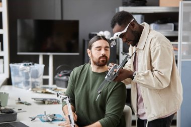 Teknoloji tamir atölyesindeki İHA 'da aksiyon kameralarını inceleyen iki kişinin portresi.