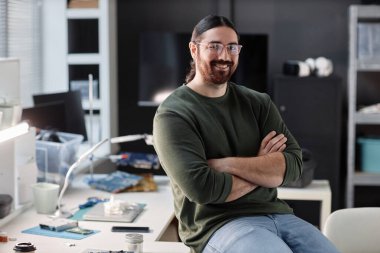 İş yerindeki teknoloji tamirhanesinde kameraya gülümseyen sakallı yetişkin bir adamın portresi.