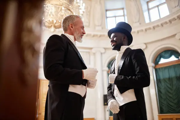 stock image Low angle view at two gentlemen wearing classic tailcoats enjoying conversation in palace hall, copy space